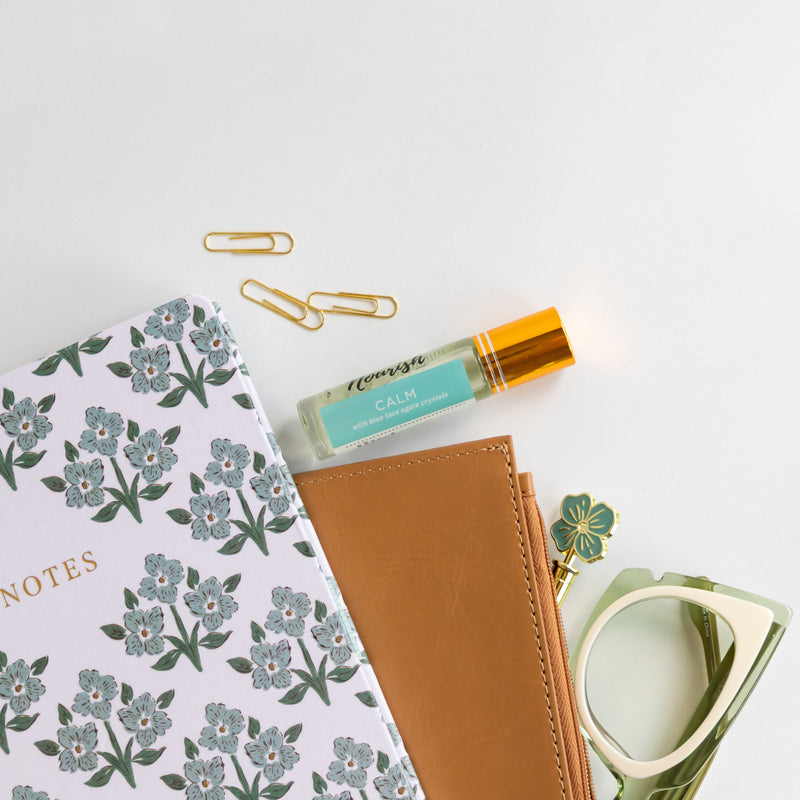 Notebook, pen, and stationery items on a marble surface with a Calm Roller Blend