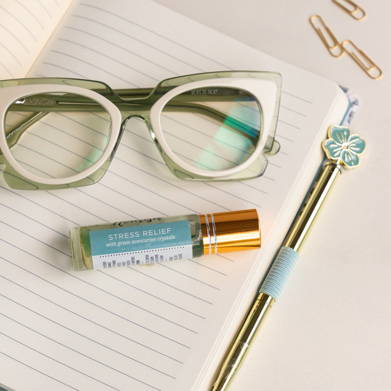 Glasses, pen, and Stress Relief Roller Blend on a notebook