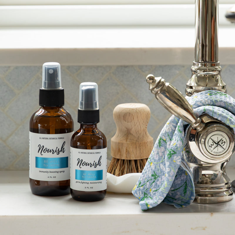 Be Well for Home and Be Well for Hands on a kitchen counter next to a sink.