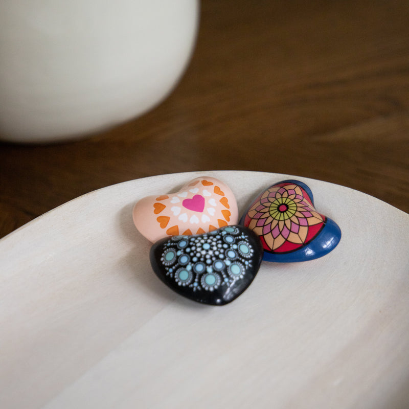 Three colorful Mandala Chime Hearts on a white surface with a blurred background