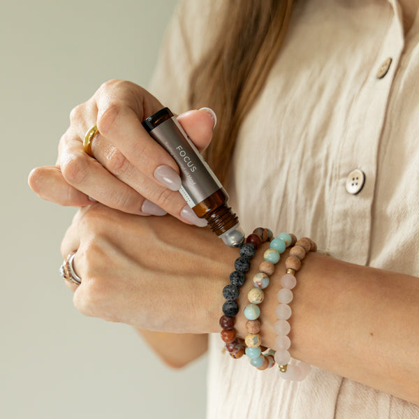 Person applying Focus Roller Blend on beaded bracelets on a neutral background