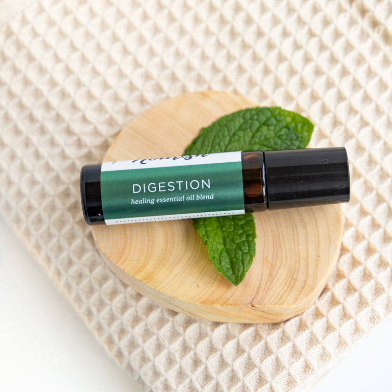 Digestion Roller Blend with mint leaves on a wooden disc and woven mat background
