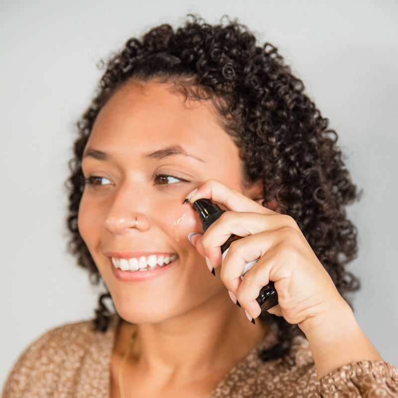 Woman applying Glow Face Serum on cheek against a plain background