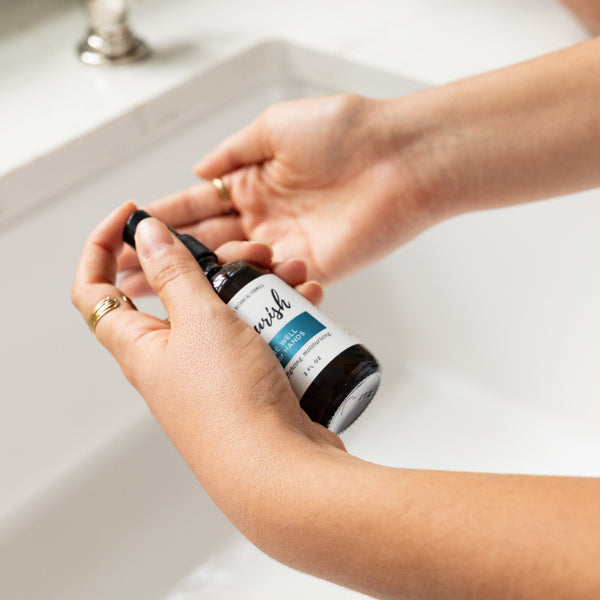 Person holding a bottle of Be Well for Hands over a sink