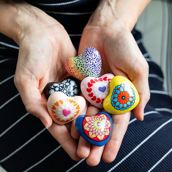 Colorful decorated Mandala Chime Hearts held in hands against a striped background