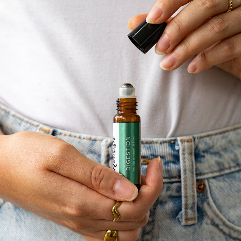 Person holding a Digestion Roller Blend against their stomach, wearing gold rings.
