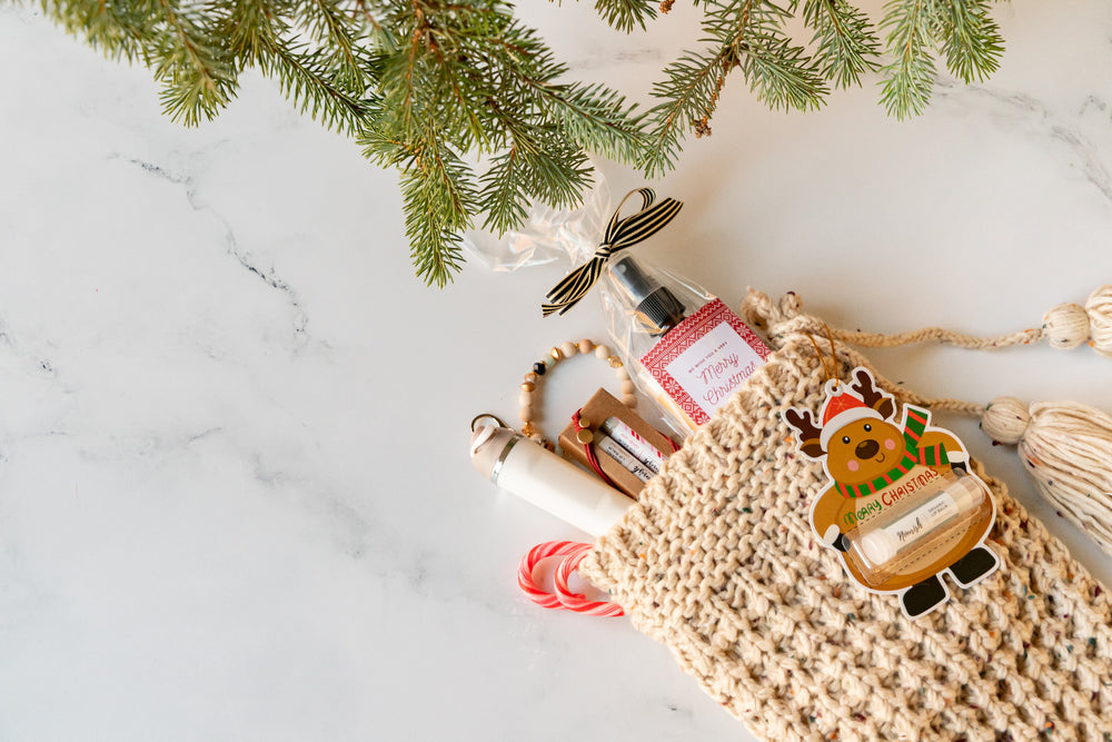 Gift bag with a bottle of perfume and a card, decorated with Christmas-themed elements on a marble surface.