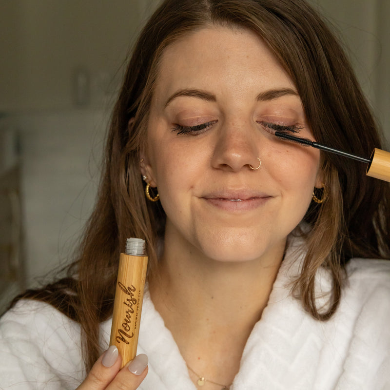 Woman holding bamboo lash serum tube and applying lash serum to eyelashes
