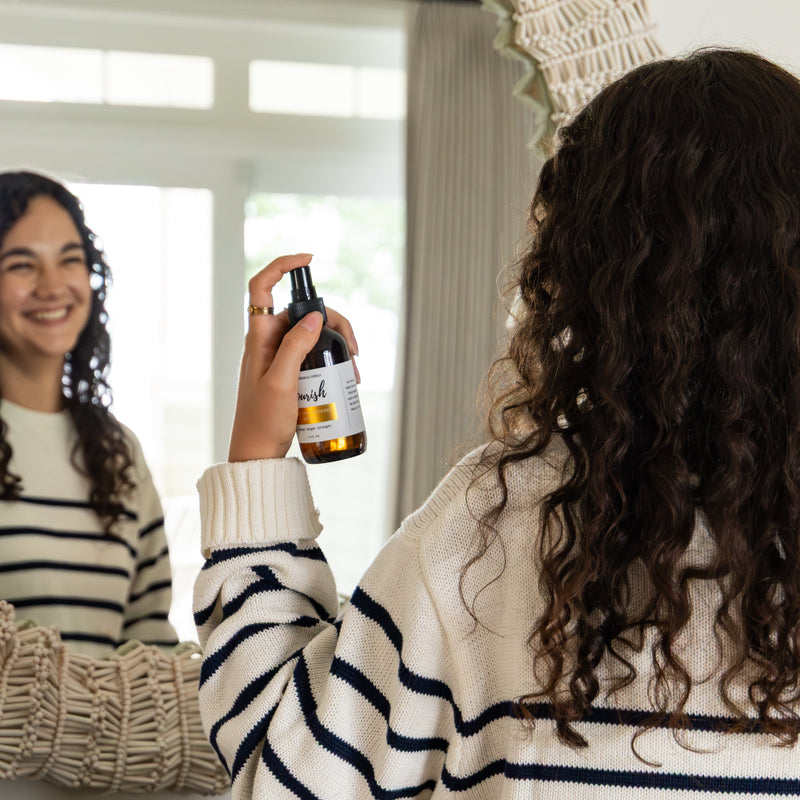 Woman applying Hair Thickening Spray in front of mirror